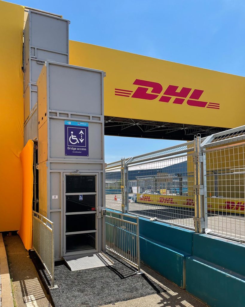 12' ADA Lift Rentals at the NYC Formula E Prix accessing a bridge to cross the race track. Yellow signage in the background.