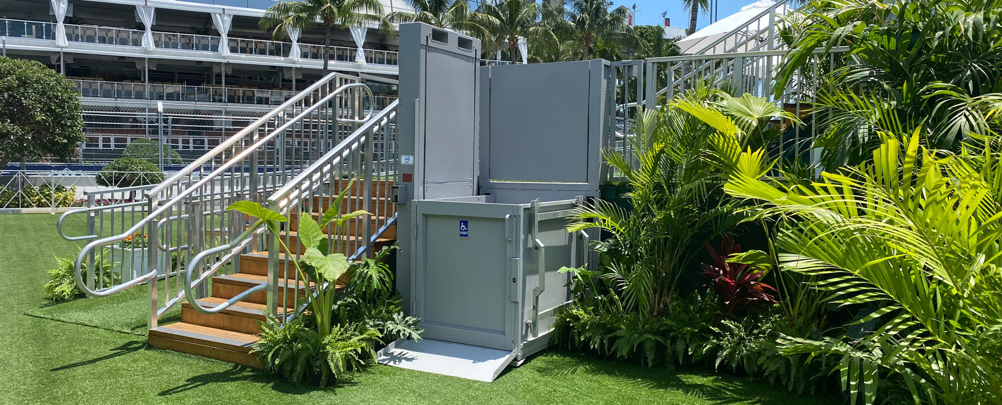 6' grey ADA wheelchair lift rental next to stairs and greenery at the Miami Grand Prix
