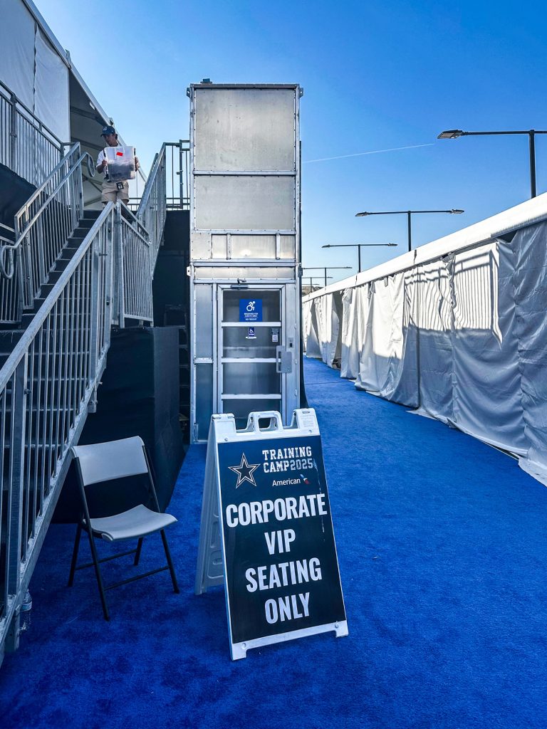 12' ADA Lift Rentals' wheelchair lift next to stairs, with Dallas Cowboys' corporate seating signage in front.
